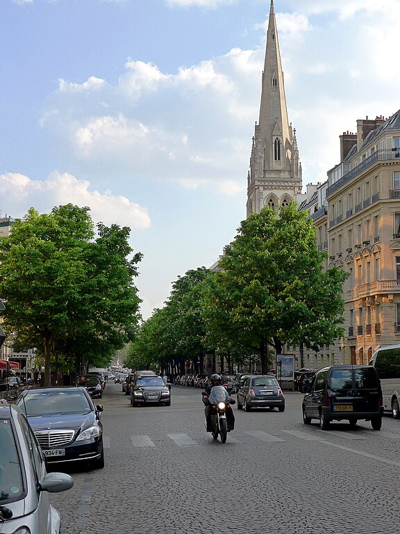 A wide paved avenue with a high church spire and a traditional Parisian townhouse