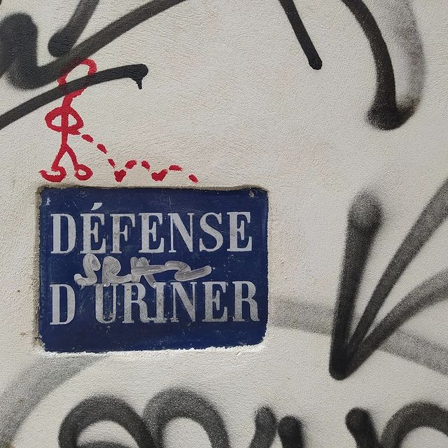 Sign on a wall, reading “Défense d'uriner”. A stick figure is graffitied above the sign, drawn urinating on it