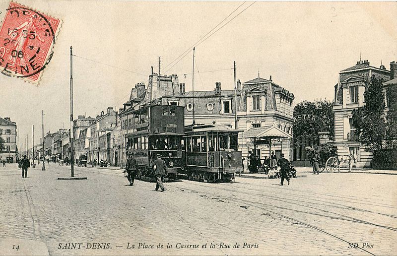 A black-and-white postcard showing Saint-Denis - La Place de la Caserne et la Rue de Paris - with two trams