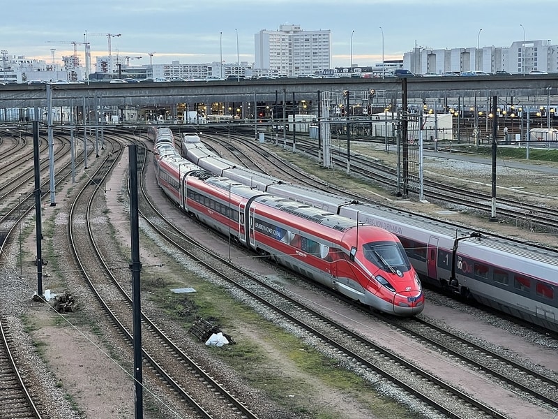 Red high-speed train and grey high-speed train on wide area of train tracks