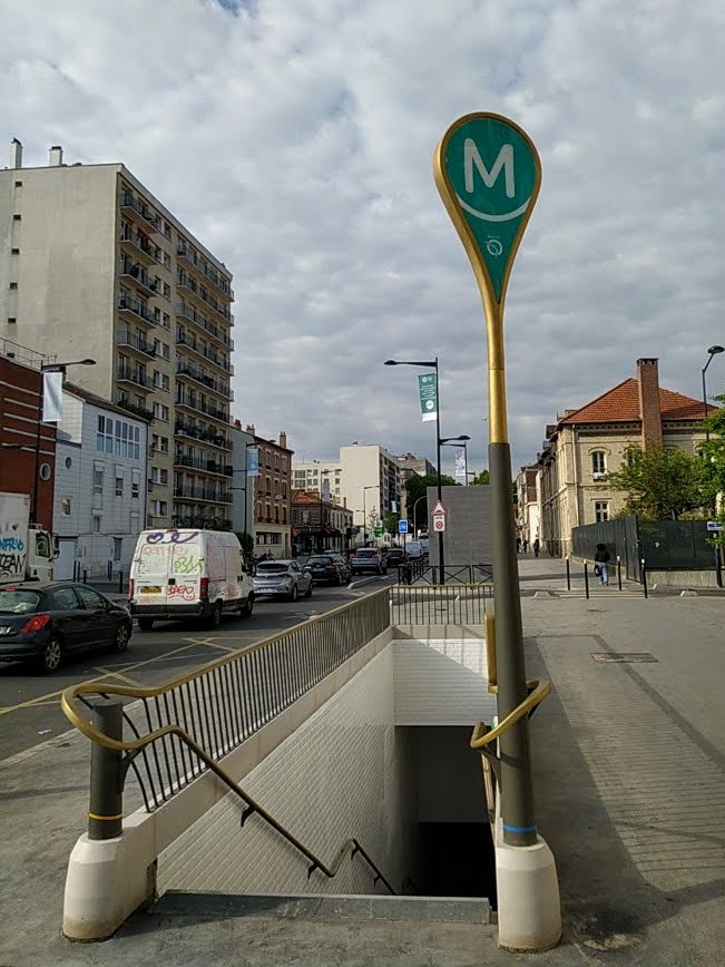 Station exit with modern sign showing the letter M on a turquoise background, with the RATP logo