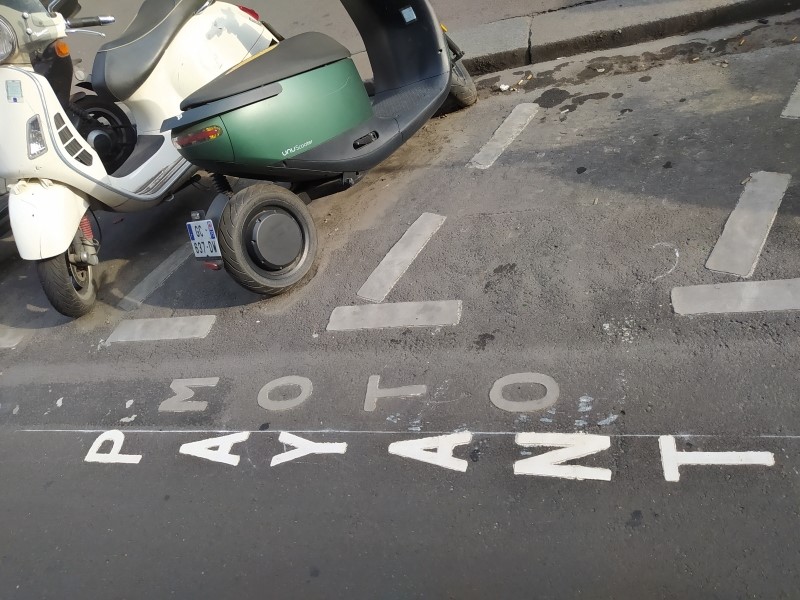 Small parking bays with motorcycles parked in them. Written in the road are the words MOTO and PAYANT. PAYANT is visibly newer, in a whiter shade