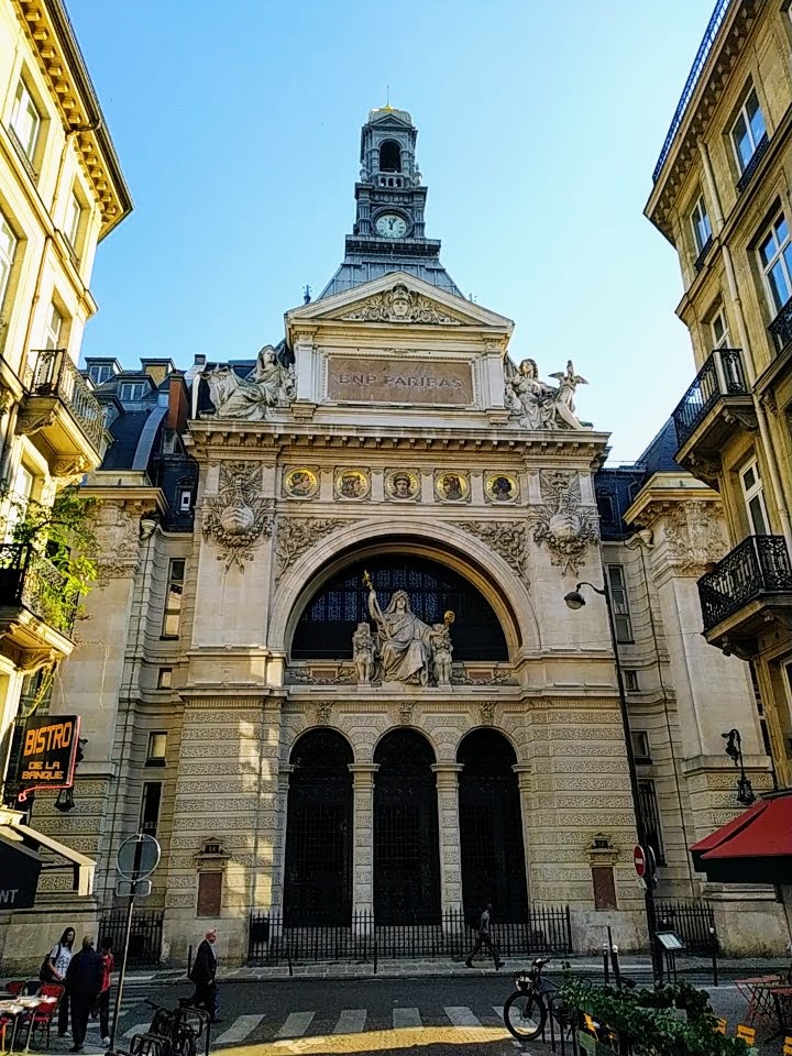Stone façade with various decorative elements. The name BNP PARIBAS is displayed near the top, under a small clock tower