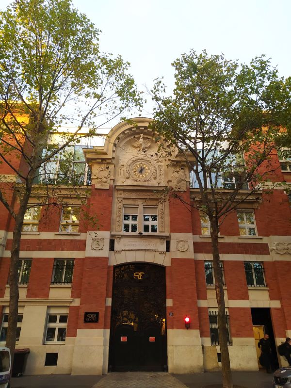 Red-brick building with light grey stone features. The letters RF are displayed in gold above the black front door; above them, on the third floor, is a clock face with black hands and golden markers