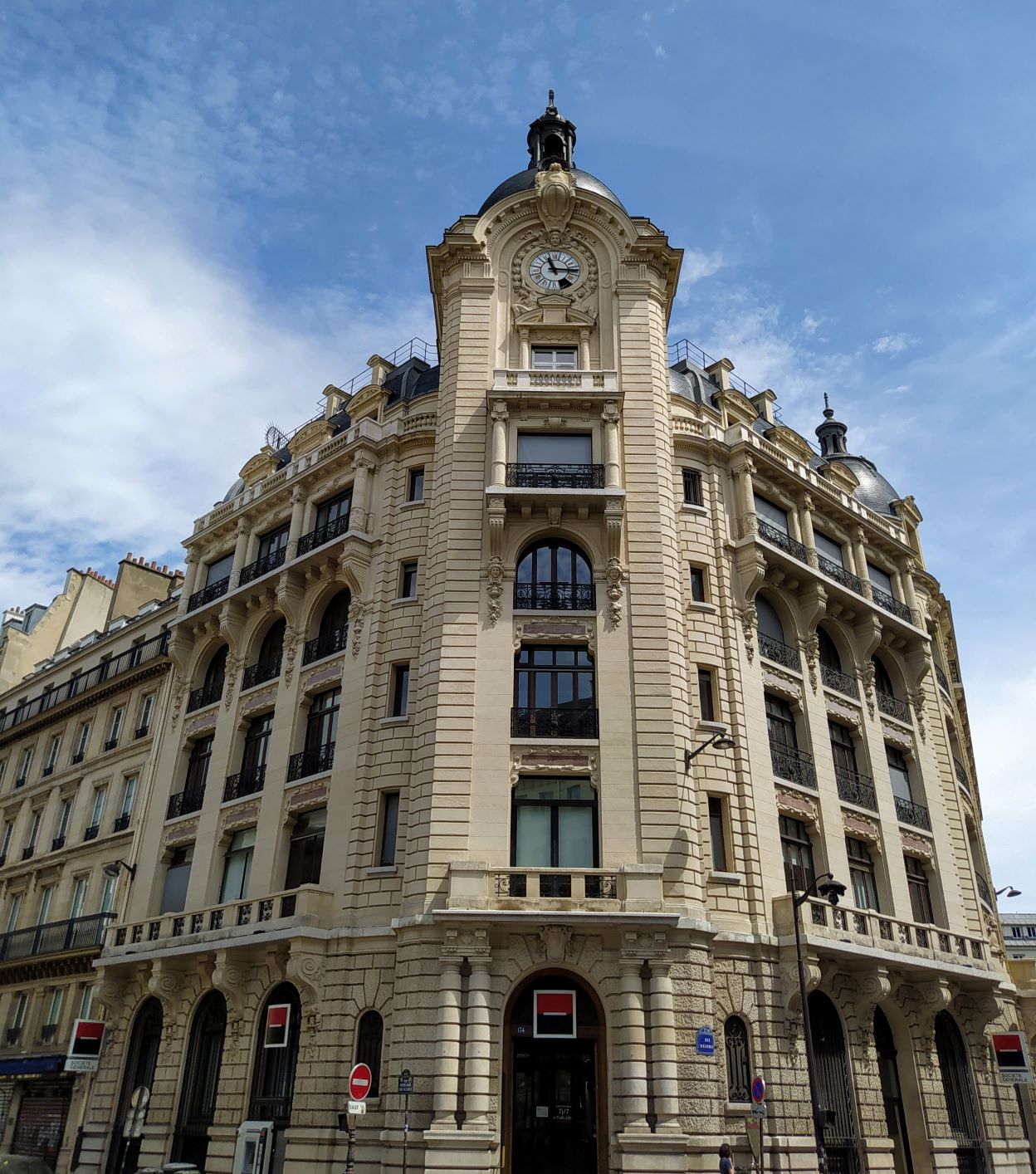 Corner terrace building with Société Générale logo showing on ground floor. A tower on the corner features a dome, with a clock at the top