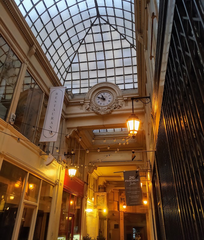 Analogue clock showing 10:49. Above is a glass roof; below is a passageway lit by traditional lights