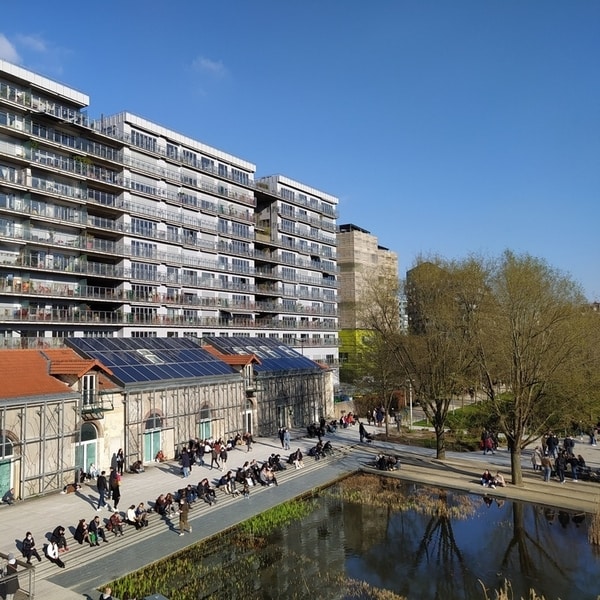 People congregating in small groups between a pond and a mid-rise building development
