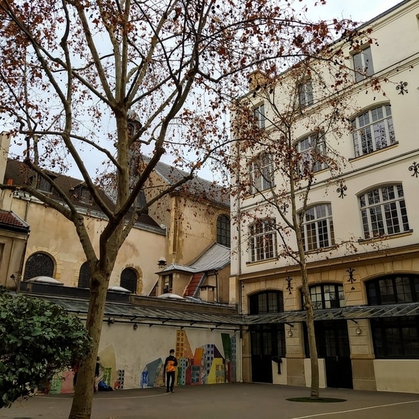 A small school courtyard with children playing on a tarmac space with two trees