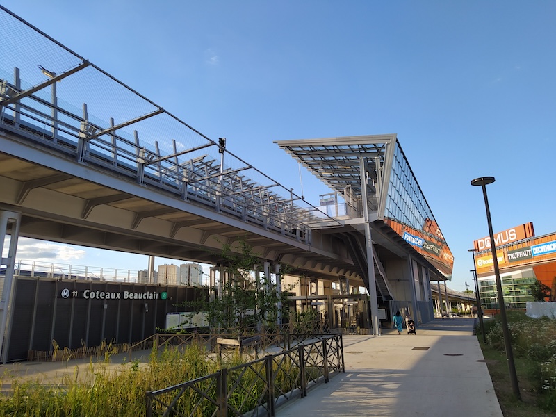 View of Coteaux Beauclair station from ground level. We can see one platform, with roof and wall of glass, reflecting adjacent shopping centre DOMUS