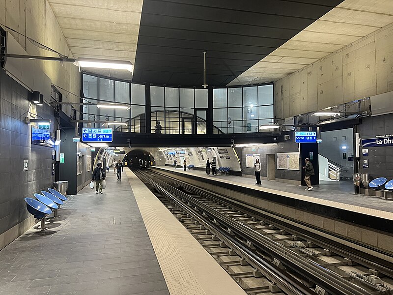 Large, well-lit station as seen from a platform. We can see a bridge over the tracks