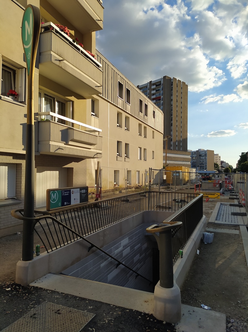 View of a metro staircase entrance, with an M mast and curved fence