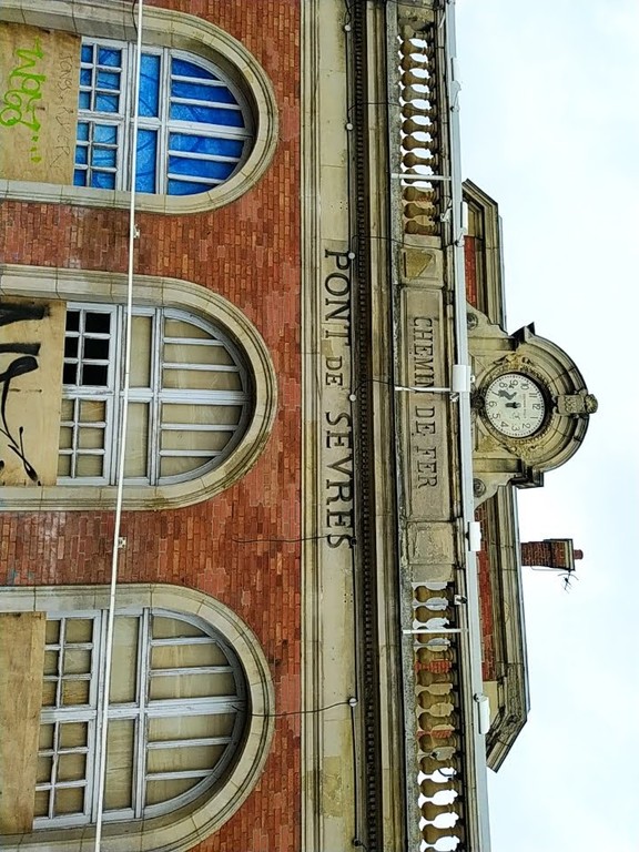 Boarded-up railway station building. Text engraved in wall: CHEMIN DE FER : PONT DE SEVRES