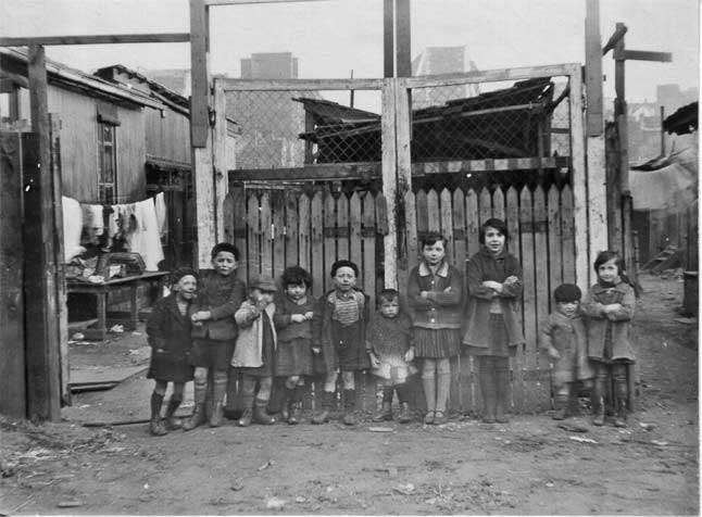 Black and white photograph of children in front of ramshackle building