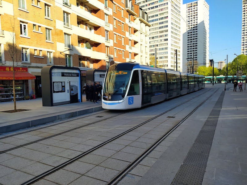 Tram at Porte de Choisy station. Behind is another tram. There are tall brick and concrete buildings in the background