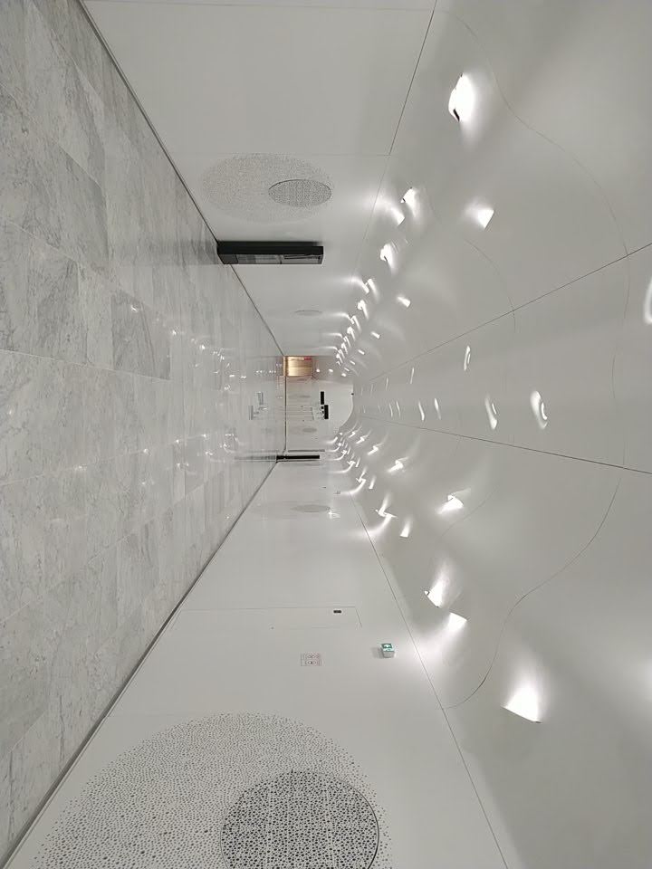 Passageway with white walls, white marble floor, and a wavy white ceiling