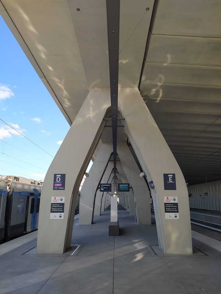 Railway platform. A train is parked on the left, while the tracks on the right sit empty