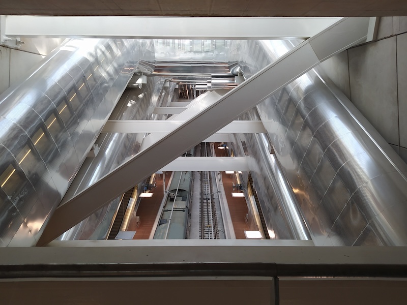 View of tracks from above. We can see the top of a train and lots of supporting beams