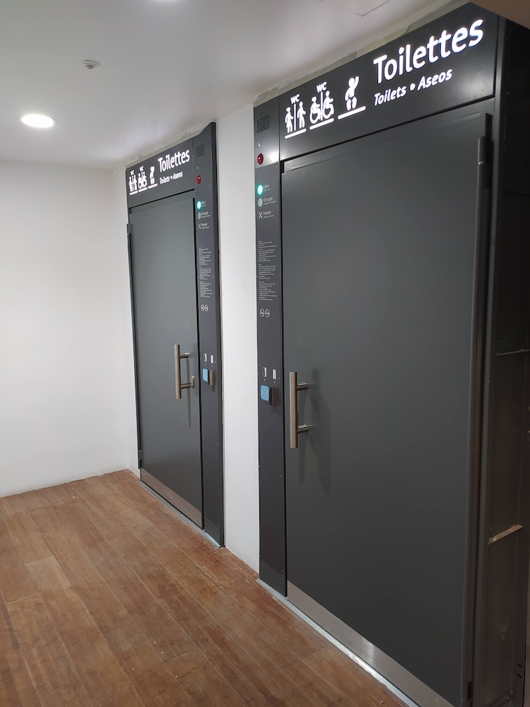 Two toilet doors. Coloured lights show whether they are available, in use or out of order. Readers for passes and tickets allow entry