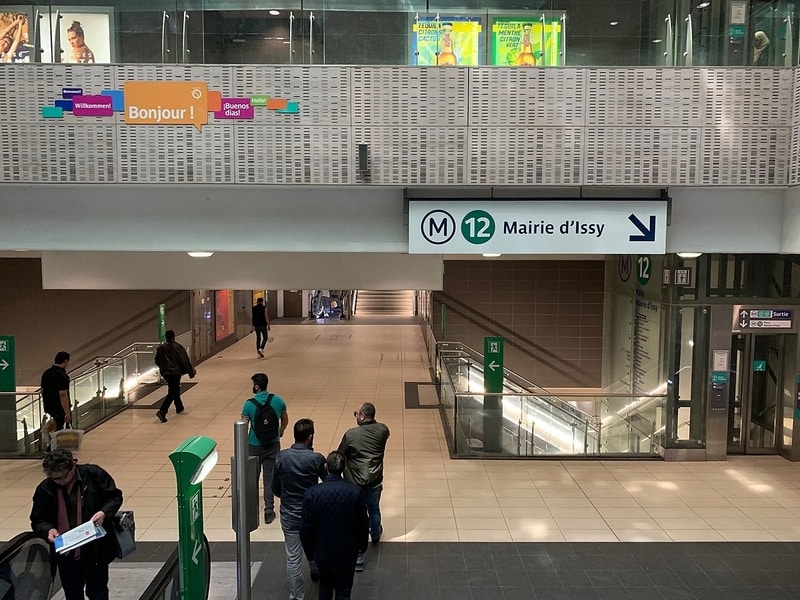 Metro station concourse, with a large sign for Mairie d'Issy and a smaller sign with welcome messages in several languages