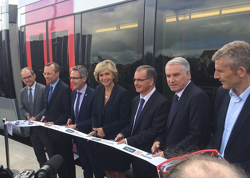 Valérie Pécresse and six grey-haired white men cut a ribbon in front of a tram-train