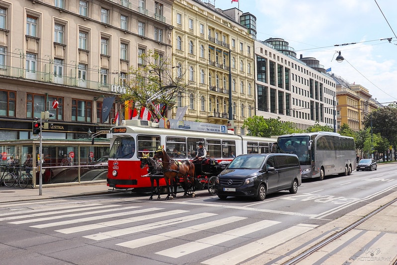 A street in Vienna with a Fiaker, a tram, a van, a coach and a car