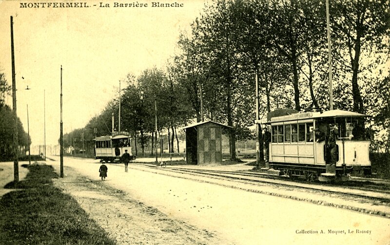A black and white photo of a road with tram tracks and two trams. Labelled MONTFERMEIL -- La Barrière Blanche. Collection A. Moquet, Le Raincy