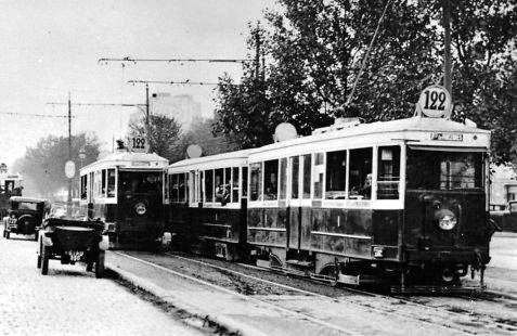 Black and white photograph of trolley trams passing. The trams appear to be on reserved tracks, with motorcars passing in a separate lane. Each tram is labelled 122