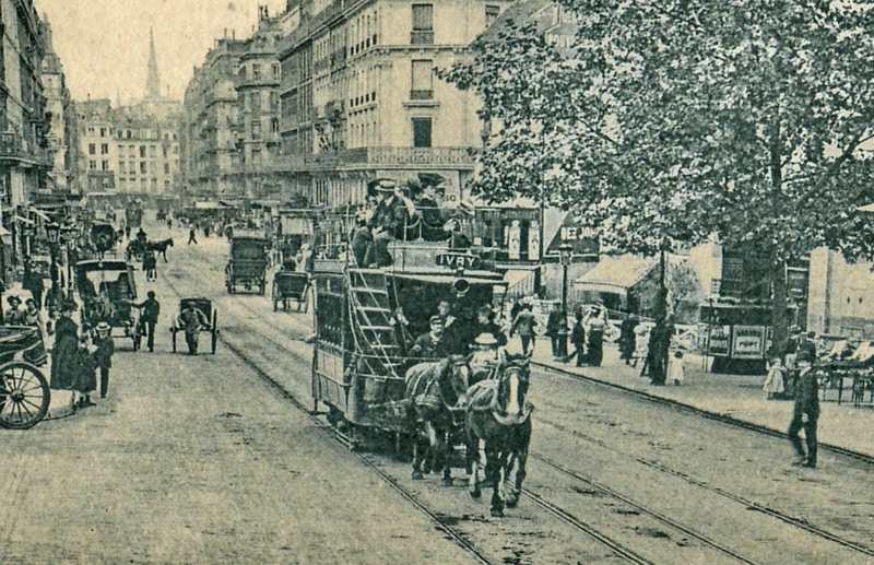 Horse-drawn tram labelled IVRY, surrounded by pedestrians and horse-drawn carriages