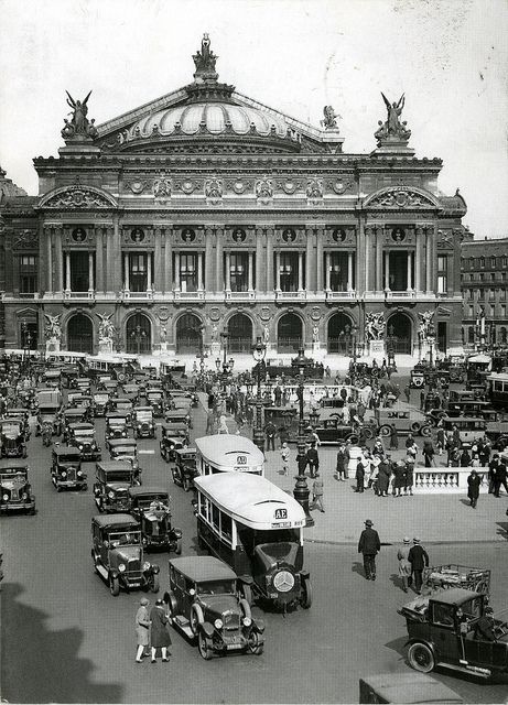 Overhead view of a six-wide queue of motorcars on the junction in front of the Opéra Garnier. In the foreground are two buses, numbered AD and AE